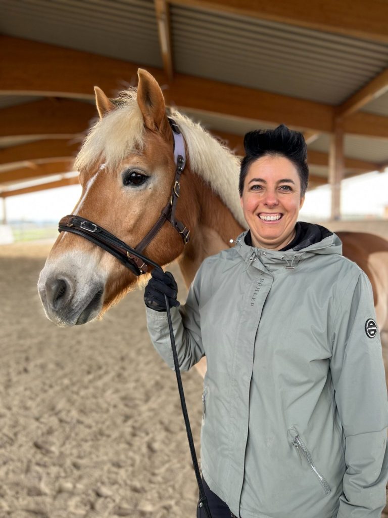 Longieren als Dialog Reiter longiert ein Pferd in einer sandigen Reitarena mit Holzdach.